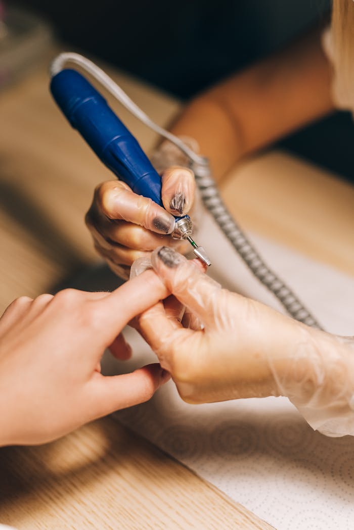 Close-up of a nail technician using an electric file during a manicure session. Ideal for beauty and fashion content.